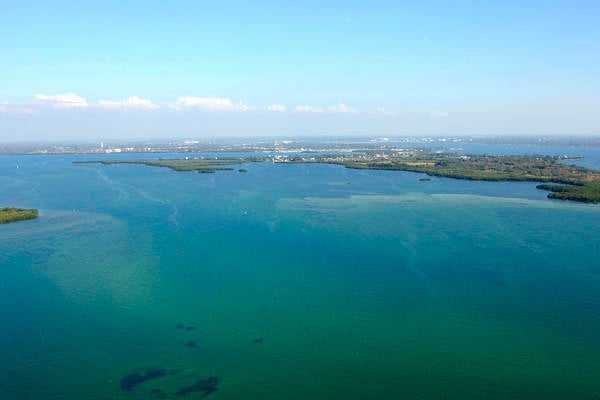 Aerial view of turquoise and blue water with scattered islands and green coastline under clear sky